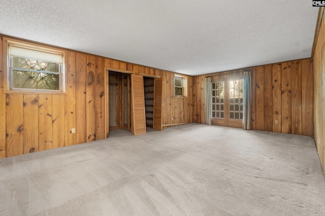 unfurnished room featuring light carpet, a textured ceiling, and wood walls