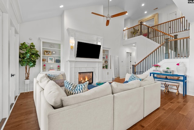 living room with built in shelves, ceiling fan, dark wood-type flooring, high vaulted ceiling, and a fireplace