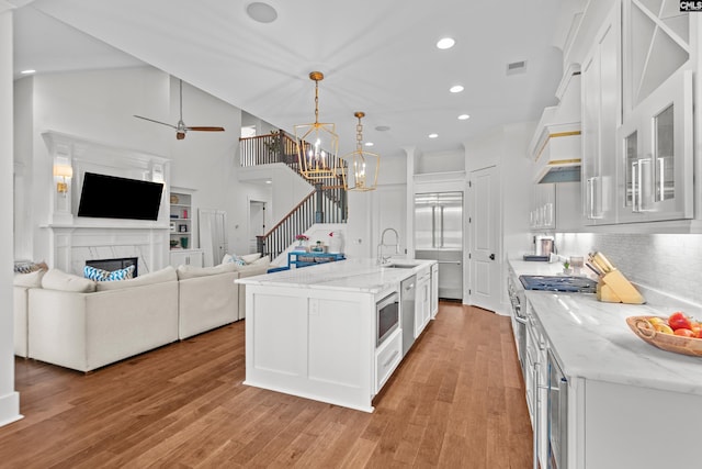 kitchen featuring tasteful backsplash, light hardwood / wood-style flooring, pendant lighting, a center island with sink, and white cabinets