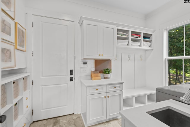 mudroom with sink, light wood-type flooring, ornamental molding, and washing machine and clothes dryer