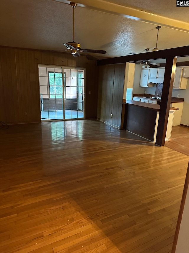 unfurnished living room with wood walls, hardwood / wood-style floors, ceiling fan, and a textured ceiling