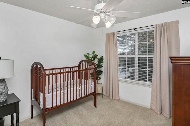 carpeted bedroom with ceiling fan, a crib, and a textured ceiling