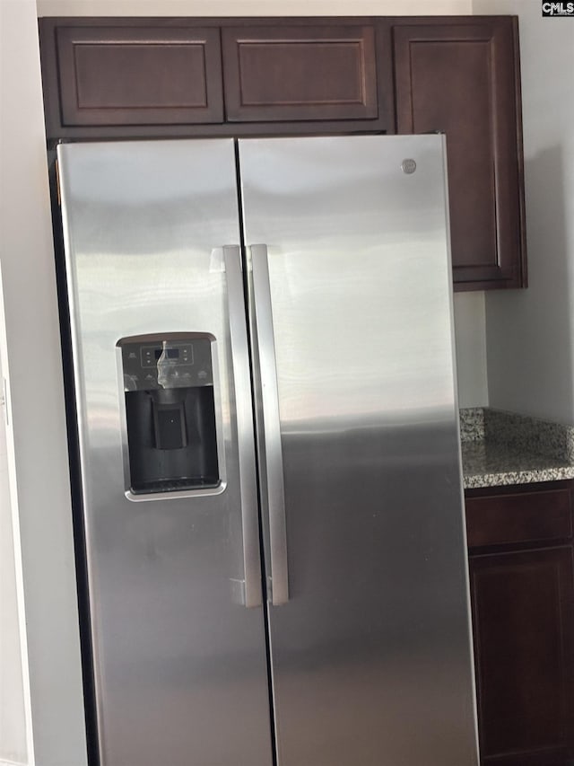 room details featuring dark brown cabinetry, light stone counters, and stainless steel fridge