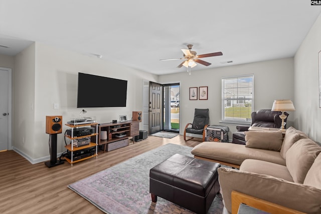 living room featuring a wood stove, ceiling fan, and light wood-type flooring