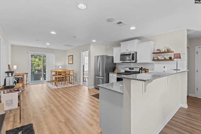 kitchen with white cabinetry, light stone counters, a kitchen bar, appliances with stainless steel finishes, and light wood-type flooring