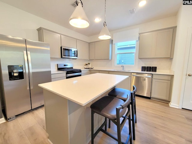 kitchen with hanging light fixtures, a kitchen island, light hardwood / wood-style floors, and appliances with stainless steel finishes