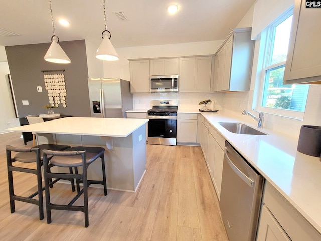 kitchen with sink, pendant lighting, light hardwood / wood-style floors, a breakfast bar area, and appliances with stainless steel finishes