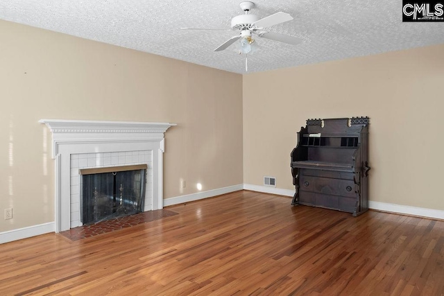 unfurnished living room featuring ceiling fan, hardwood / wood-style floors, a tile fireplace, and a textured ceiling