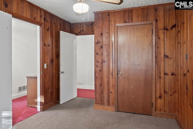 unfurnished bedroom with ceiling fan, wooden walls, a textured ceiling, and carpet flooring