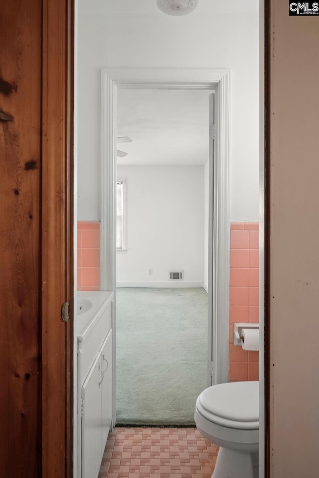 bathroom featuring toilet, tile walls, and vanity