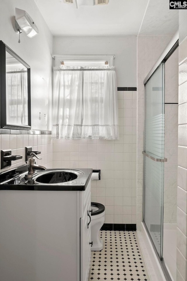 bathroom with tile patterned flooring, a shower with door, vanity, tile walls, and toilet