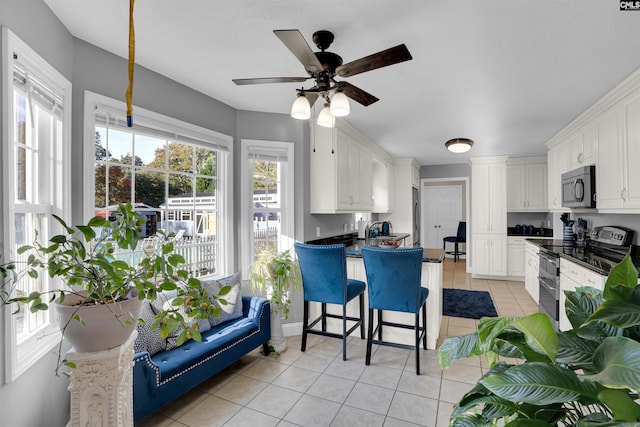 kitchen featuring a kitchen breakfast bar, ceiling fan, electric stove, light tile patterned floors, and white cabinetry