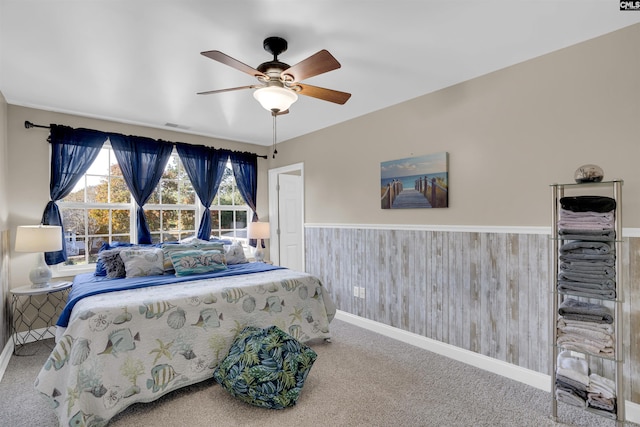 carpeted bedroom featuring ceiling fan and wooden walls