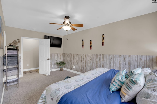 carpeted bedroom with ceiling fan and wood walls