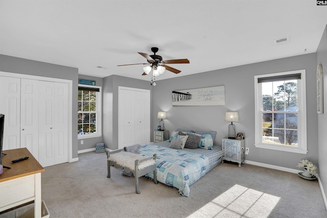 carpeted bedroom featuring ceiling fan and multiple closets