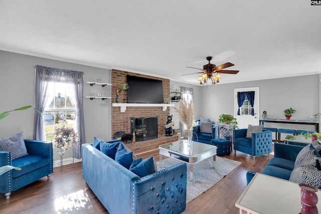 living room featuring ceiling fan, crown molding, dark wood-type flooring, and a brick fireplace