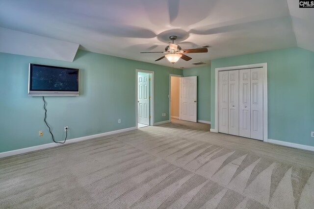 unfurnished bedroom with ceiling fan, a closet, light colored carpet, and vaulted ceiling