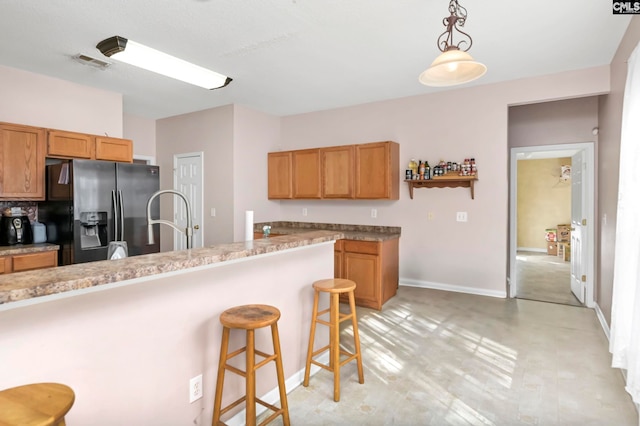 kitchen featuring a breakfast bar area, hanging light fixtures, and stainless steel refrigerator with ice dispenser