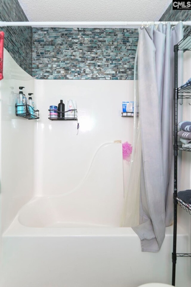 bathroom with a textured ceiling and shower / bathtub combination with curtain