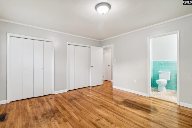 unfurnished bedroom with light hardwood / wood-style floors, tile walls, connected bathroom, and multiple closets