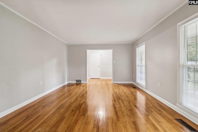 spare room featuring wood-type flooring, crown molding, and a healthy amount of sunlight