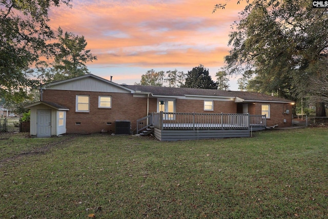 back house at dusk with a yard, central AC, a storage unit, and a wooden deck