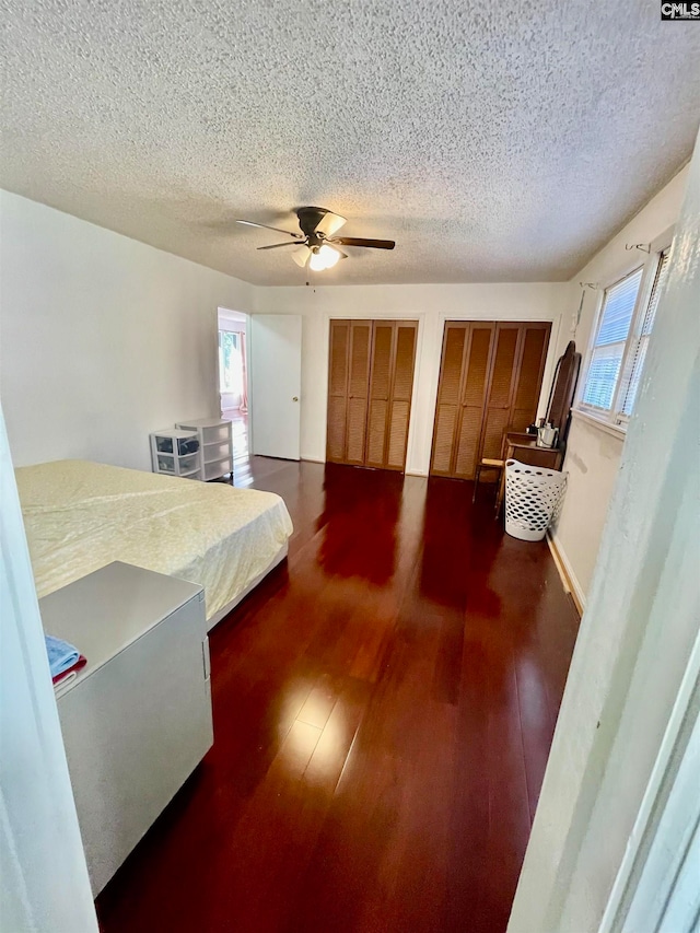 bedroom with multiple closets, ceiling fan, dark hardwood / wood-style flooring, and a textured ceiling