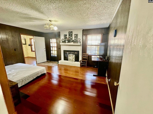 bedroom featuring hardwood / wood-style floors, wood walls, a textured ceiling, and an inviting chandelier