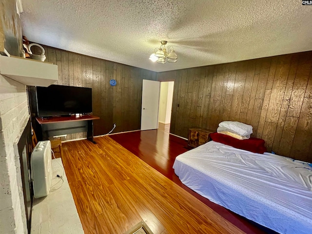 bedroom with wood walls, an inviting chandelier, a textured ceiling, and hardwood / wood-style flooring