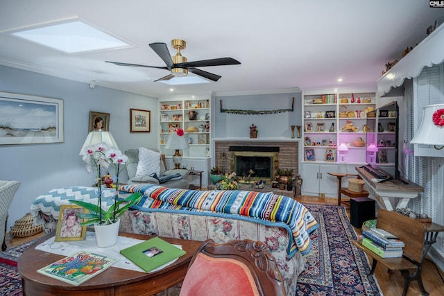 living room with a skylight, ceiling fan, a brick fireplace, wood-type flooring, and ornamental molding