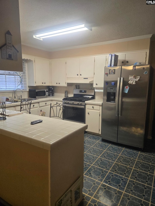 kitchen featuring appliances with stainless steel finishes, tile countertops, white cabinetry, and ornamental molding