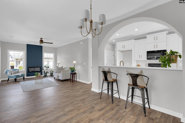 kitchen featuring crown molding, wood-type flooring, a breakfast bar area, white cabinets, and ceiling fan with notable chandelier