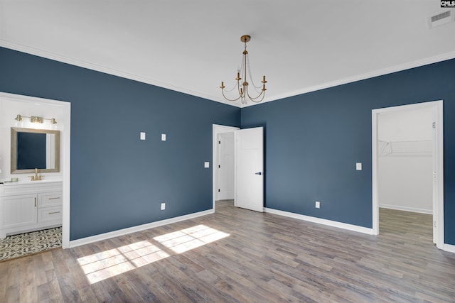 interior space featuring a walk in closet, ensuite bath, ornamental molding, light hardwood / wood-style flooring, and a chandelier