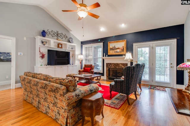 living room featuring light hardwood / wood-style flooring, high vaulted ceiling, a premium fireplace, and ceiling fan