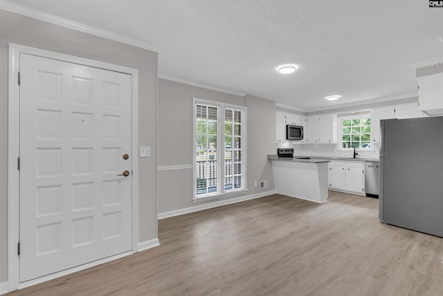 kitchen featuring white cabinets, light wood-type flooring, ornamental molding, appliances with stainless steel finishes, and a textured ceiling