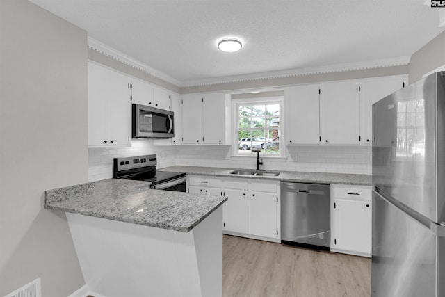 kitchen with sink, stainless steel appliances, light stone counters, kitchen peninsula, and white cabinets