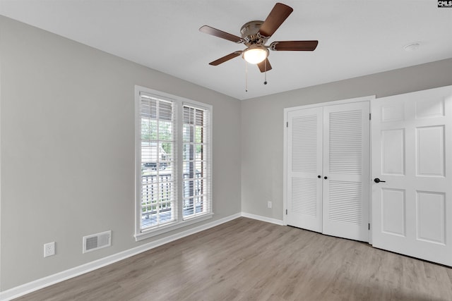 unfurnished bedroom with light wood-type flooring, a closet, multiple windows, and ceiling fan