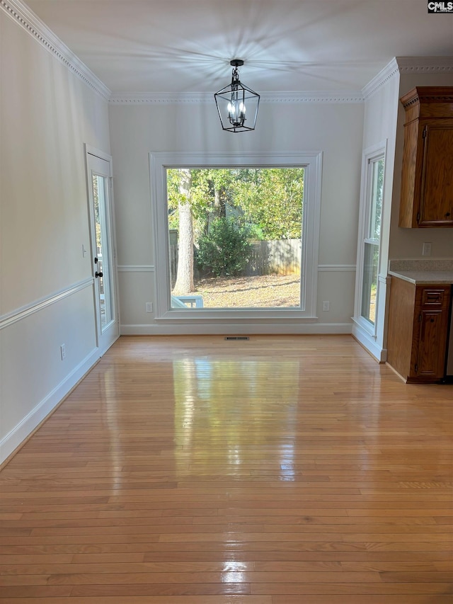 unfurnished dining area with a chandelier, light wood-type flooring, and ornamental molding