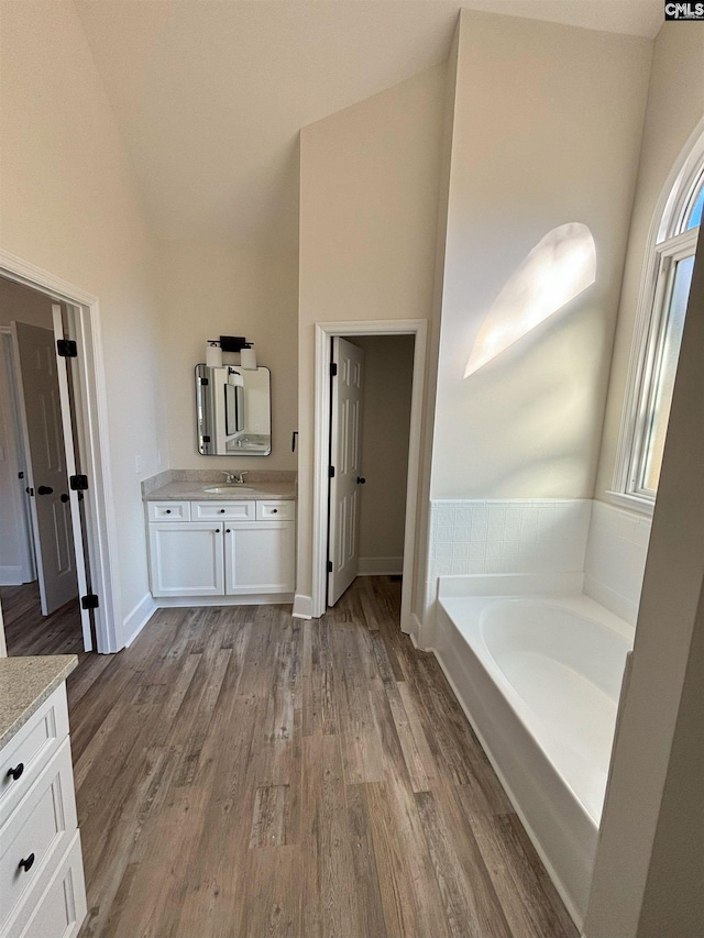 bathroom featuring vanity, wood-type flooring, a tub to relax in, and high vaulted ceiling