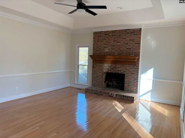 unfurnished living room with light wood-type flooring, ornamental molding, a raised ceiling, ceiling fan, and a fireplace