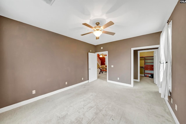 unfurnished bedroom featuring light carpet, a walk in closet, a closet, and ceiling fan