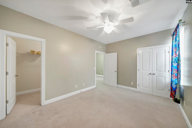 unfurnished bedroom with ceiling fan, a walk in closet, and light carpet