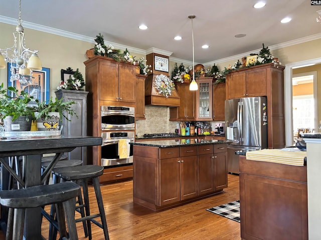 kitchen with dark stone counters, stainless steel appliances, crown molding, pendant lighting, and light hardwood / wood-style floors