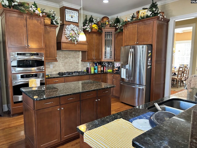 kitchen featuring stainless steel appliances, crown molding, dark stone counters, light hardwood / wood-style floors, and decorative backsplash