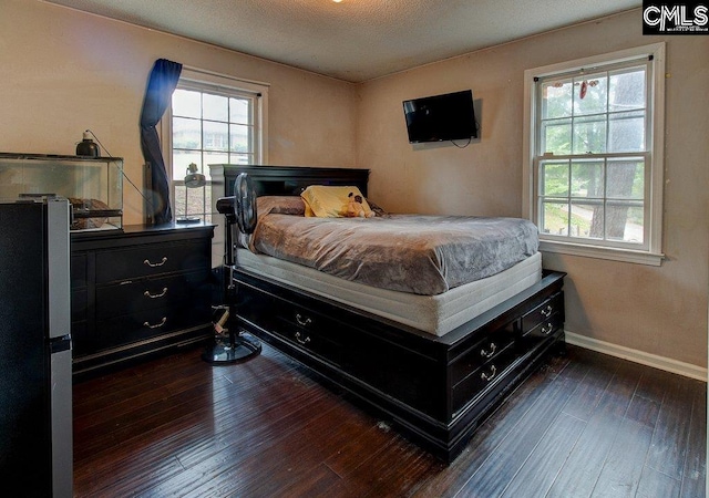 bedroom featuring a textured ceiling, refrigerator, multiple windows, and dark wood-type flooring