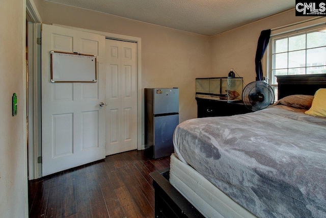 bedroom featuring a textured ceiling, stainless steel refrigerator, a closet, and dark wood-type flooring