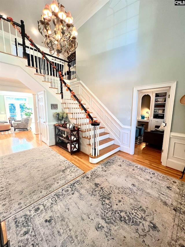 stairs featuring hardwood / wood-style flooring, a notable chandelier, crown molding, and a high ceiling