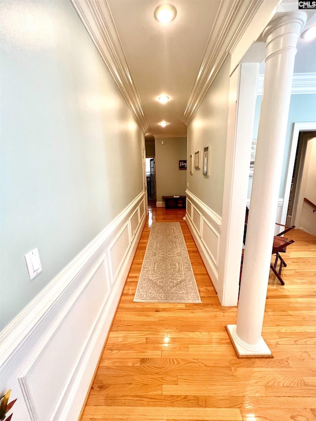 corridor featuring light wood-type flooring, decorative columns, and crown molding