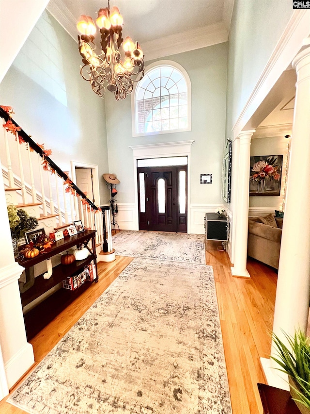 foyer featuring a high ceiling, crown molding, ornate columns, light hardwood / wood-style floors, and a chandelier