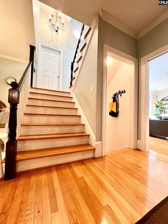 staircase with hardwood / wood-style flooring, a notable chandelier, and crown molding